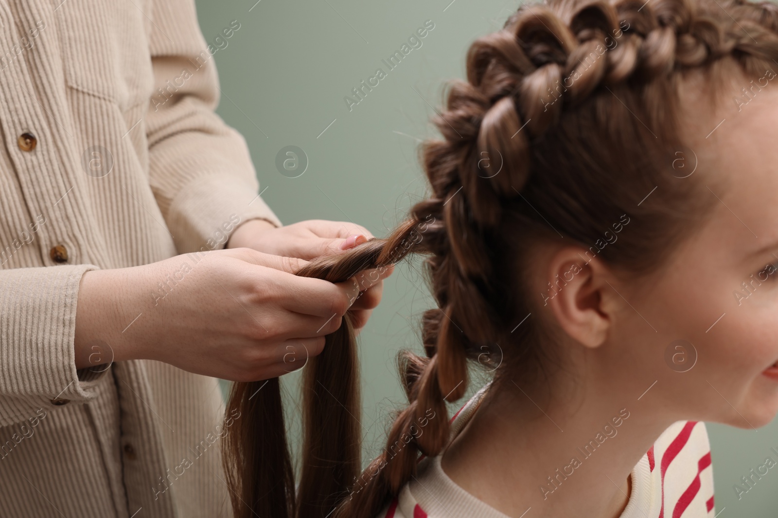 Photo of Professional stylist braiding woman's hair on olive background, closeup