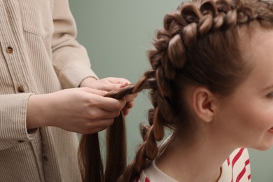 Professional stylist braiding woman's hair on olive background, closeup