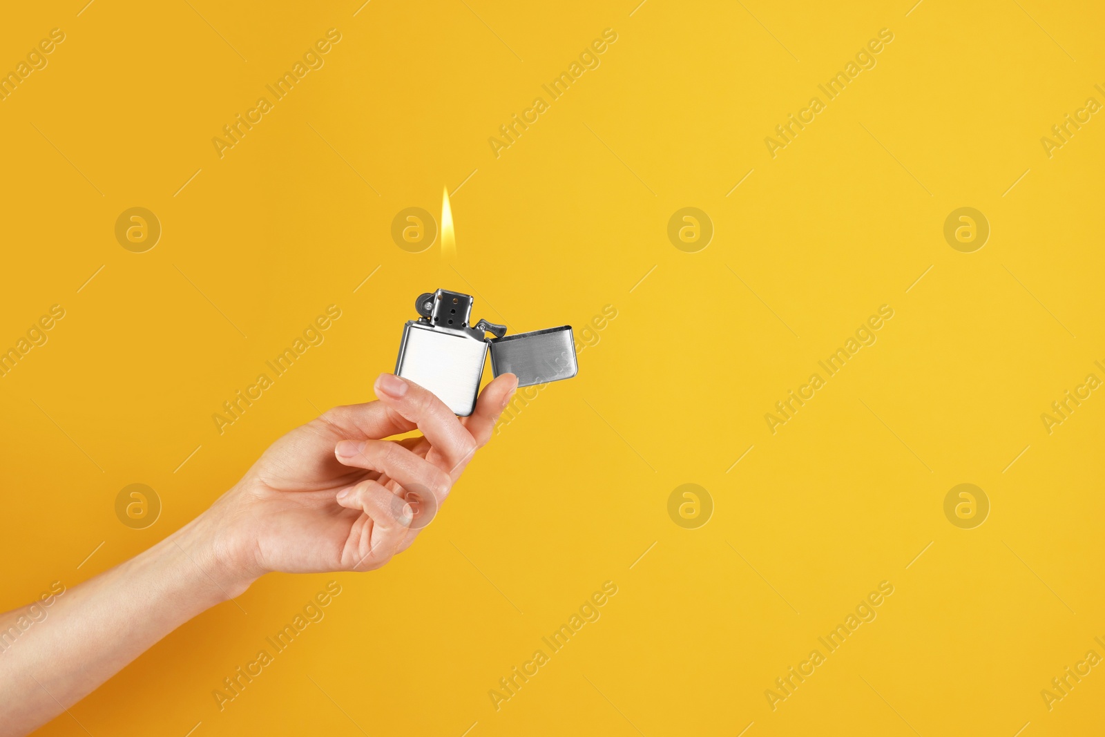 Photo of Woman holding lighter with burning flame on orange background, closeup. Space for text