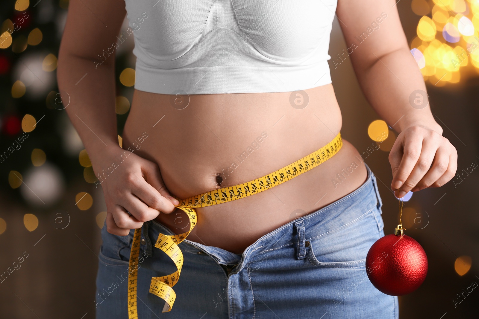 Photo of Woman with Christmas ball and measuring tape indoors, closeup. Overweight problem after New Year party