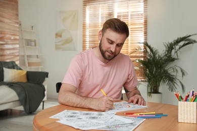 Photo of Young man coloring antistress picture at table indoors