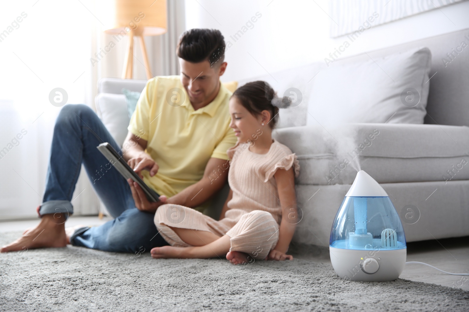 Photo of Father and daughter with tablet near modern air humidifier at home