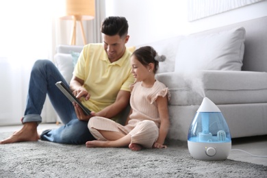 Photo of Father and daughter with tablet near modern air humidifier at home