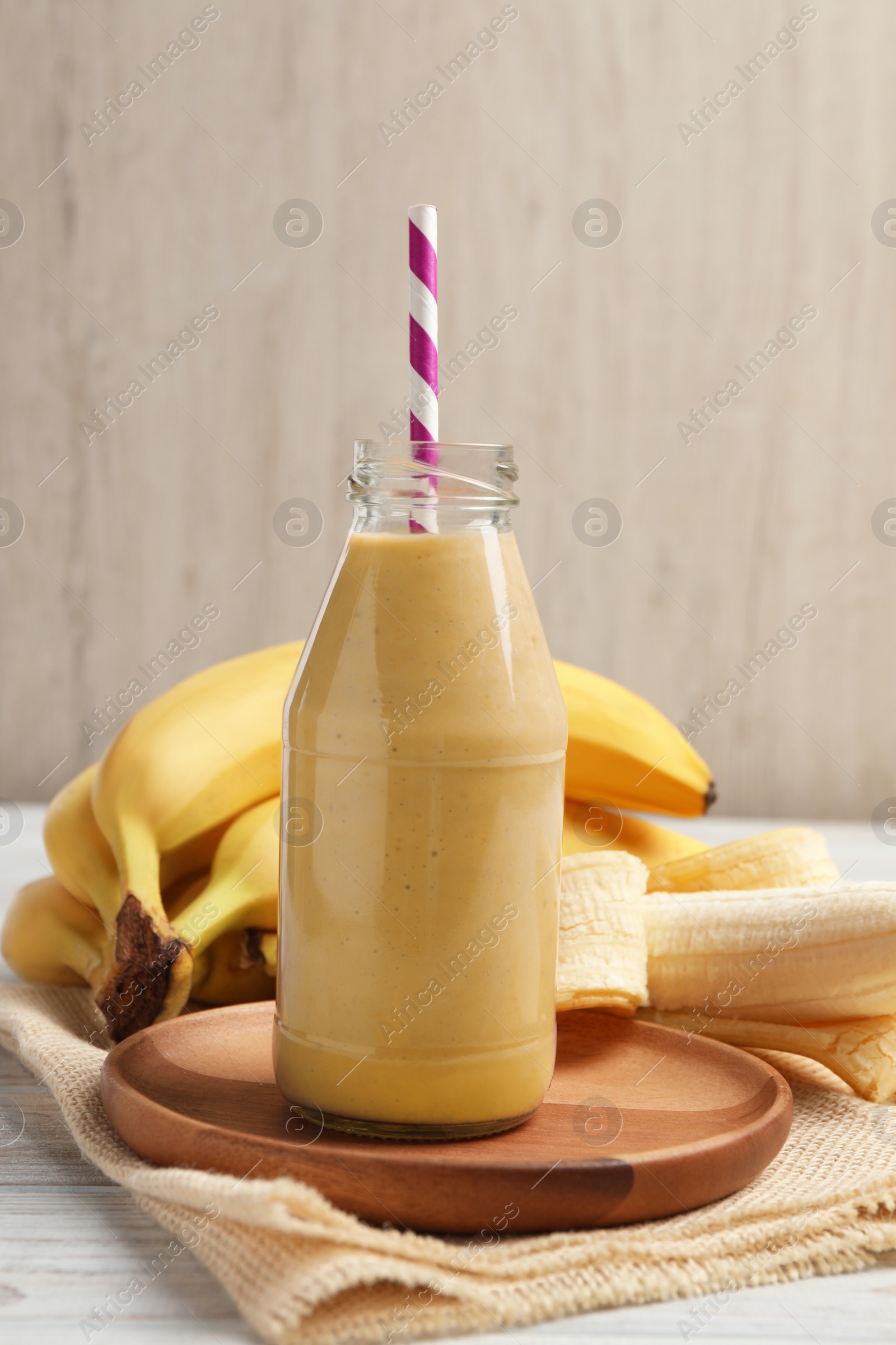 Photo of Bottle of tasty banana smoothie with straw and fresh fruits on white wooden table