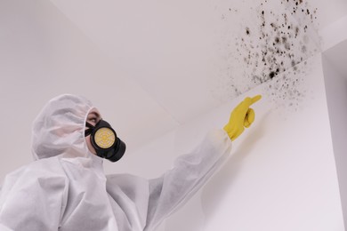 Woman in protective suit pointing at walls affected with mold