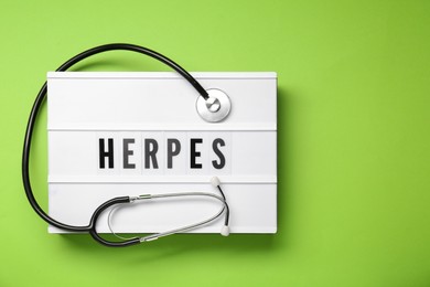 Photo of Light box with word Herpes and stethoscope on green background, top view. Space for text