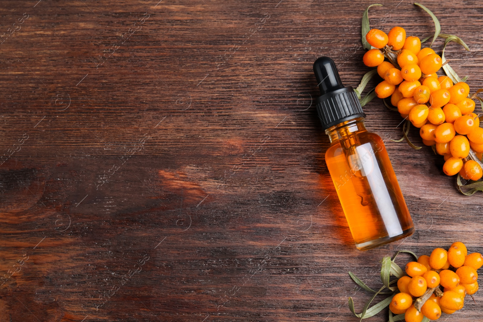 Photo of Ripe sea buckthorn and bottle of essential oil on wooden table, flat lay. Space for text