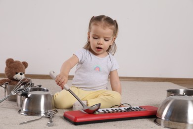 Photo of Cute little girl with cookware and toy piano at home
