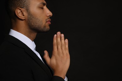 Photo of African American man with clasped hands praying to God on black background. Space for text