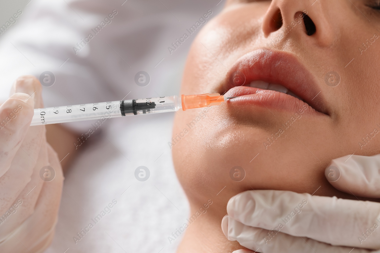 Photo of Doctor giving lips injection to young woman in clinic, closeup. Cosmetic surgery