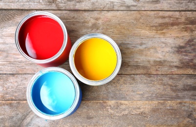 Tin cans with paint on wooden background, top view