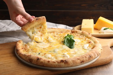 Woman taking piece of delicious cheese pizza at wooden table, closeup