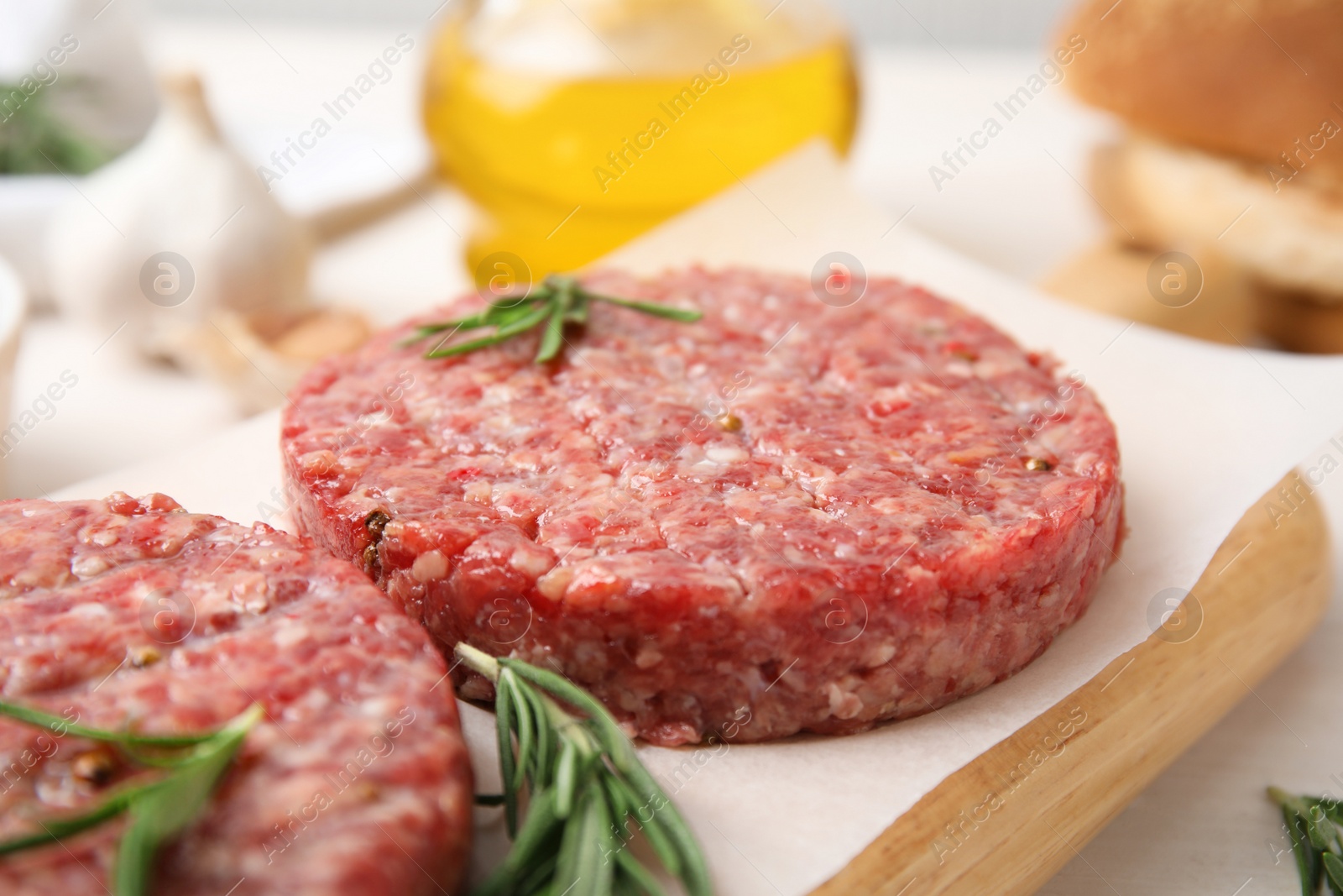 Photo of Raw hamburger patties with rosemary on wooden board, closeup