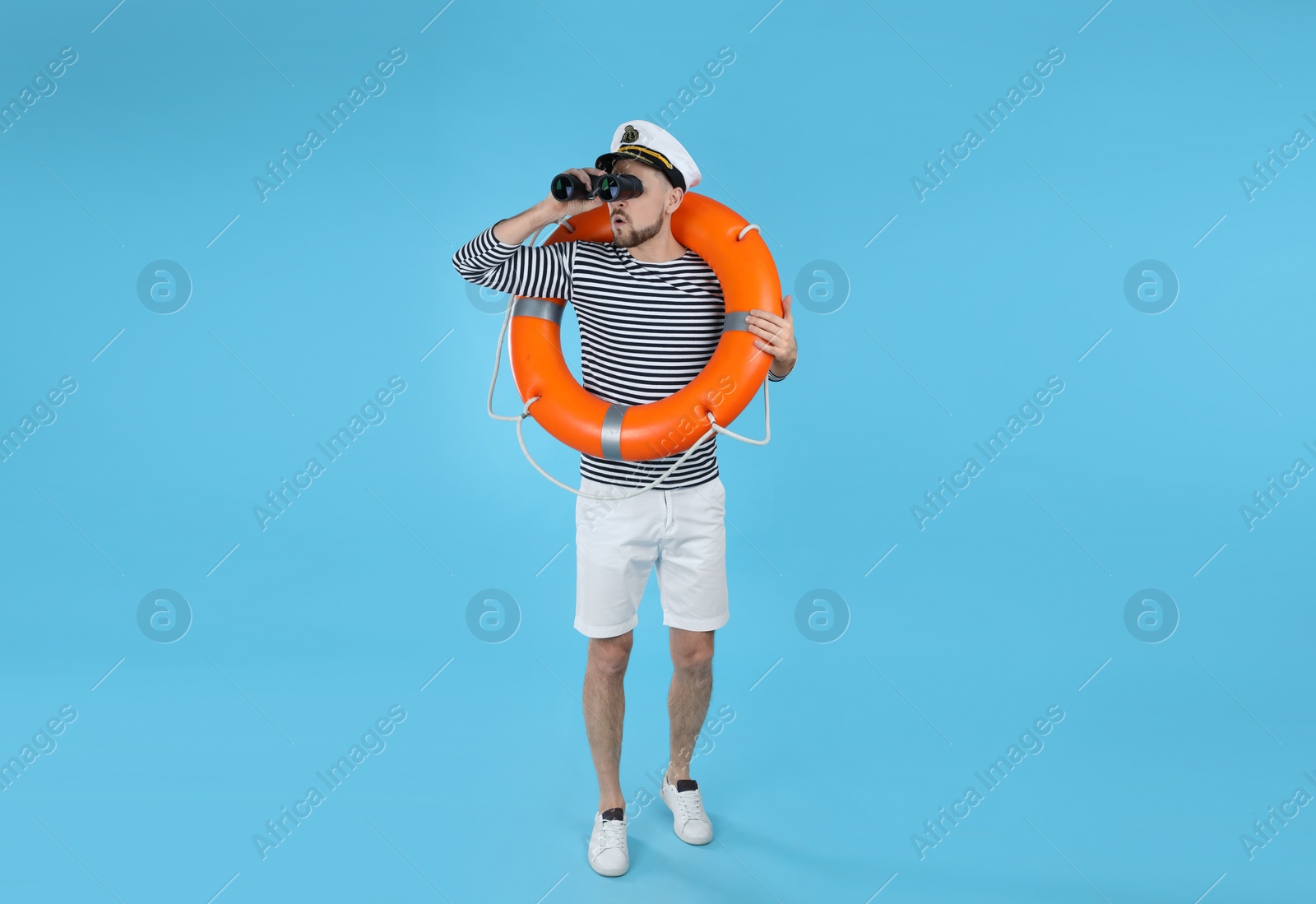 Photo of Sailor with orange ring buoy looking through binoculars on light blue background