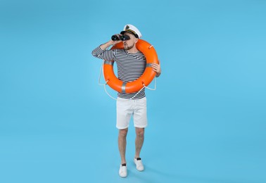 Sailor with orange ring buoy looking through binoculars on light blue background