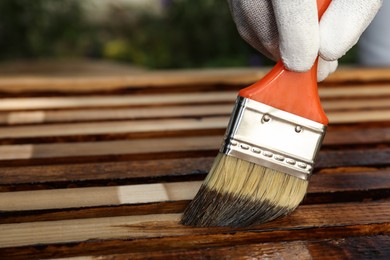 Photo of Worker applying wood stain onto planks outdoors, closeup. Space for text