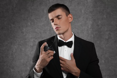 Photo of Handsome young man using perfume on grey stone background