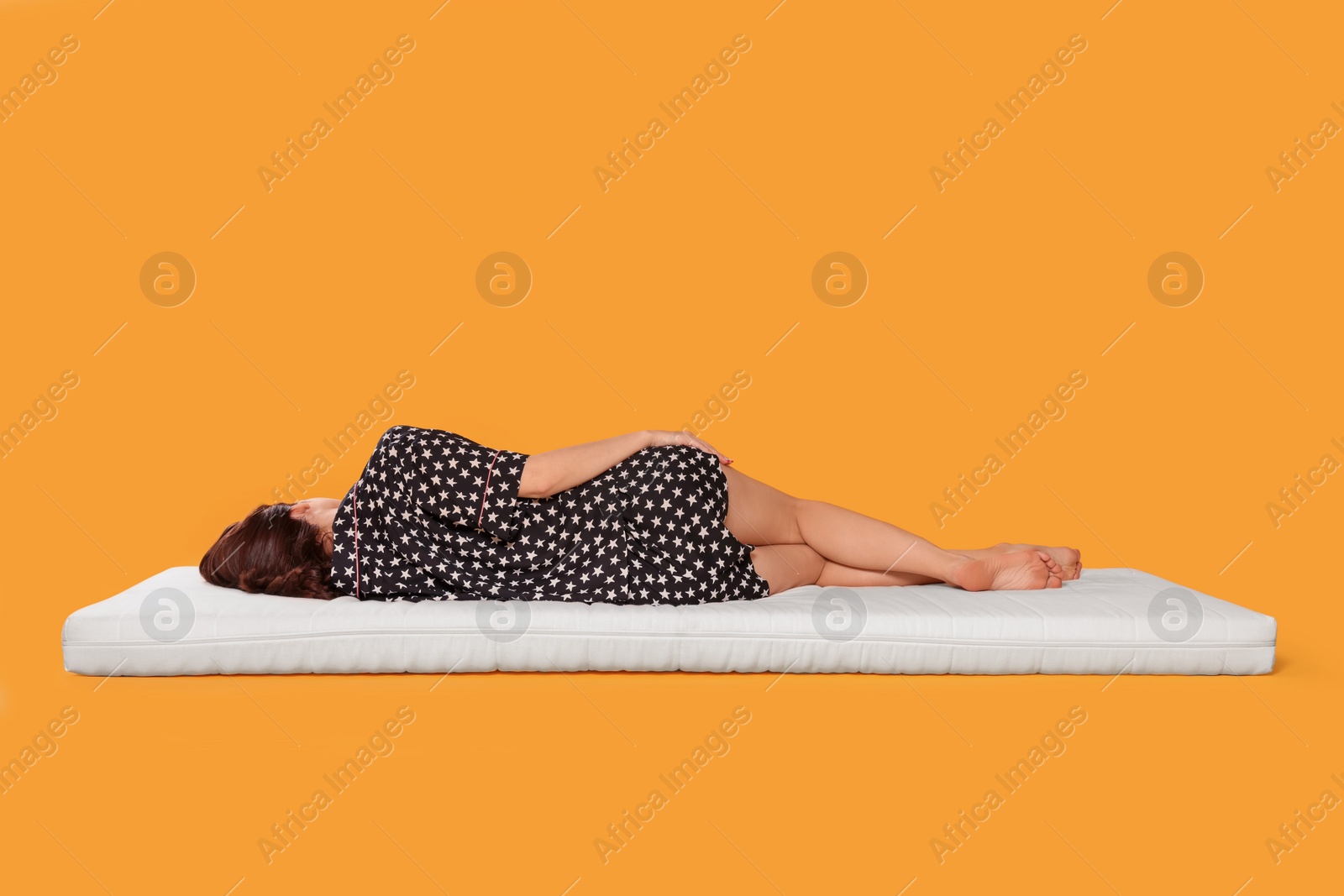 Photo of Young woman sleeping on soft mattress against orange background, back view