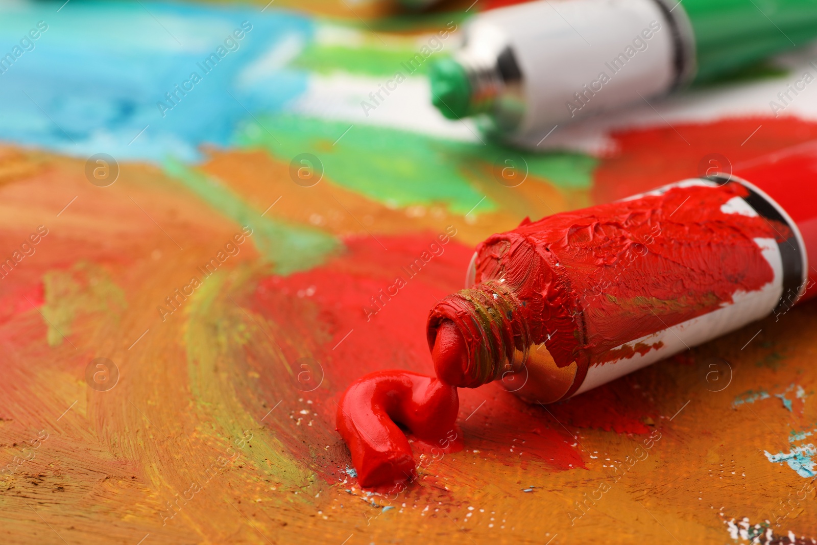 Photo of Tube of red oil paint on canvas with abstract painting, closeup