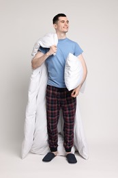 Happy man in pyjama with blanket and pillow on light grey background