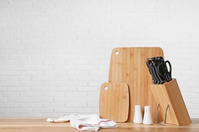 Photo of Holder with knives and clean boards on table against white brick wall. Space for text