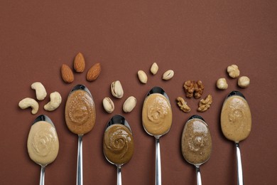 Tasty nut butters in spoons and raw nuts on brown table, flat lay. Space for text