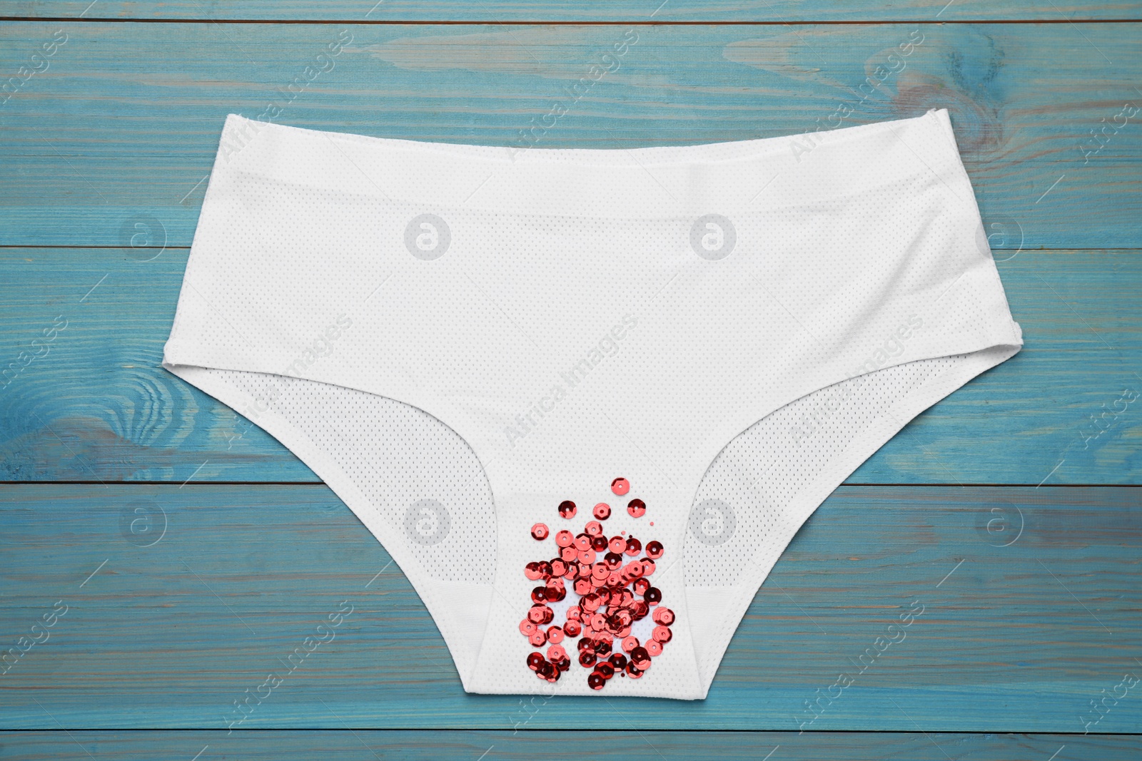 Photo of Woman's panties with red sequins on turquoise wooden background, top view. Menstrual cycle