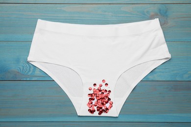 Woman's panties with red sequins on turquoise wooden background, top view. Menstrual cycle