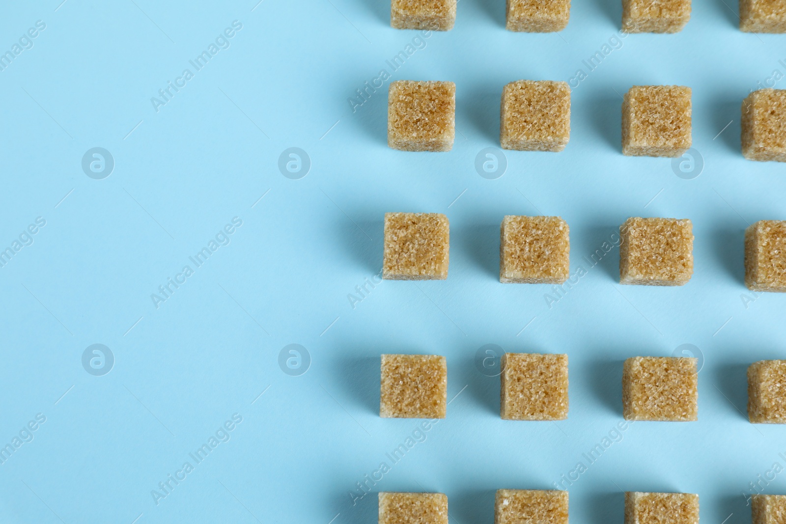 Photo of Brown sugar cubes on light blue background, flat lay. Space for text