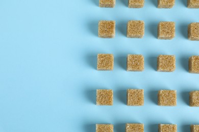 Photo of Brown sugar cubes on light blue background, flat lay. Space for text