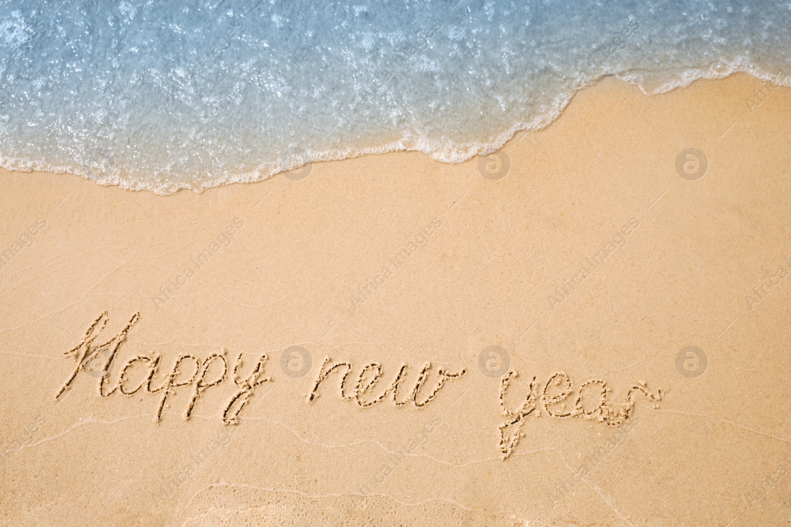 Photo of Sandy beach with text Happy New Year washed by sea, top view