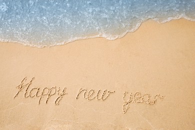 Photo of Sandy beach with text Happy New Year washed by sea, top view