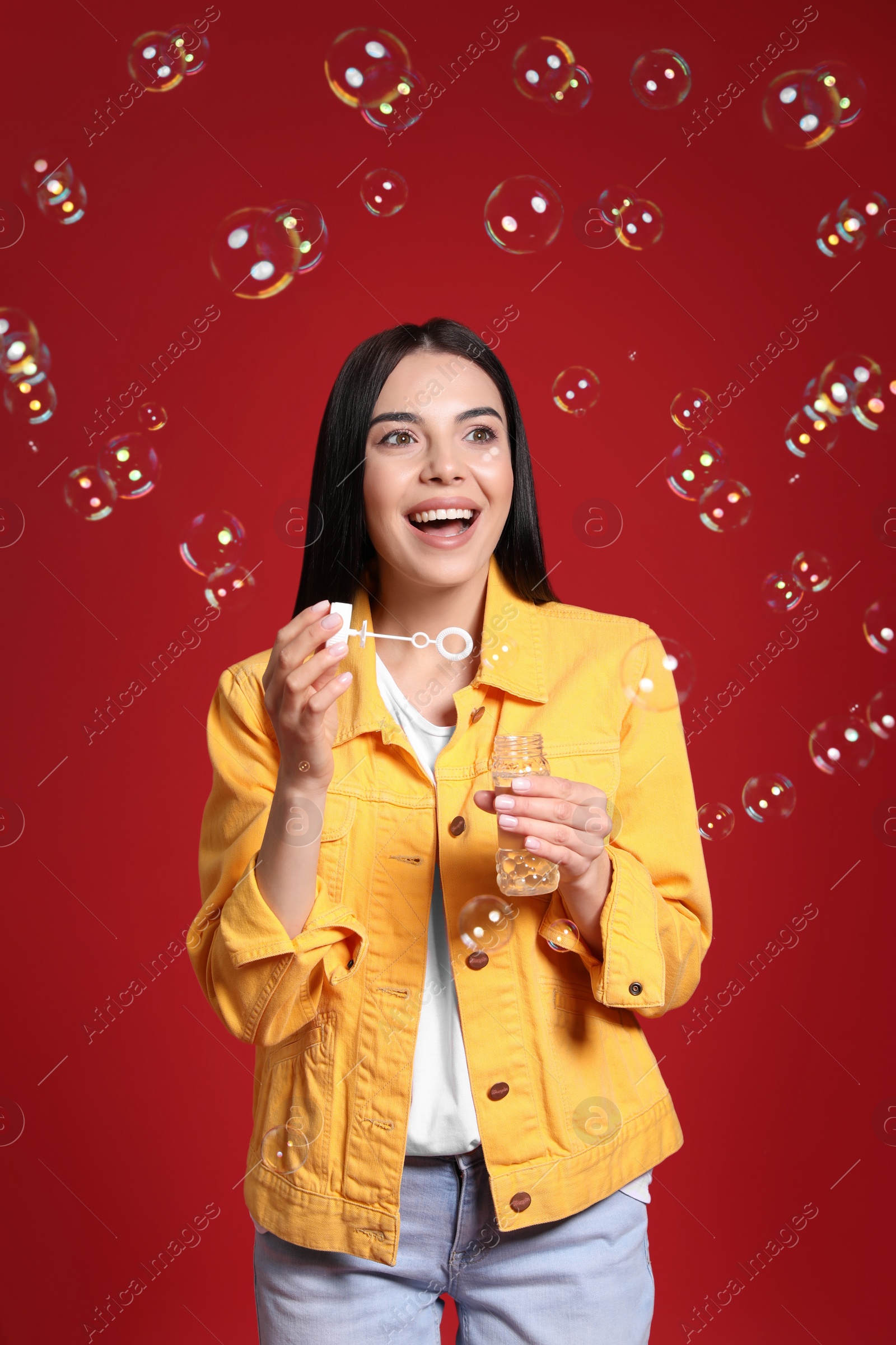 Photo of Young woman blowing soap bubbles on red background