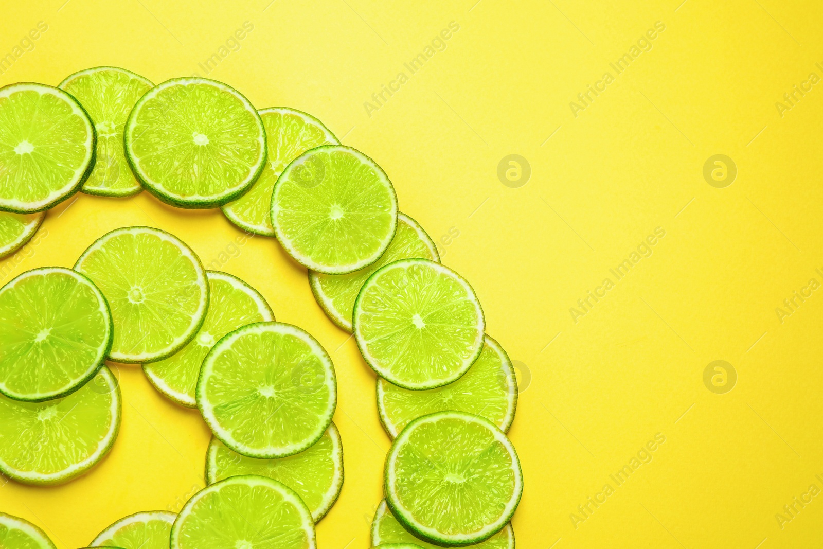 Photo of Juicy fresh lime slices on yellow background, flat lay. Space for text