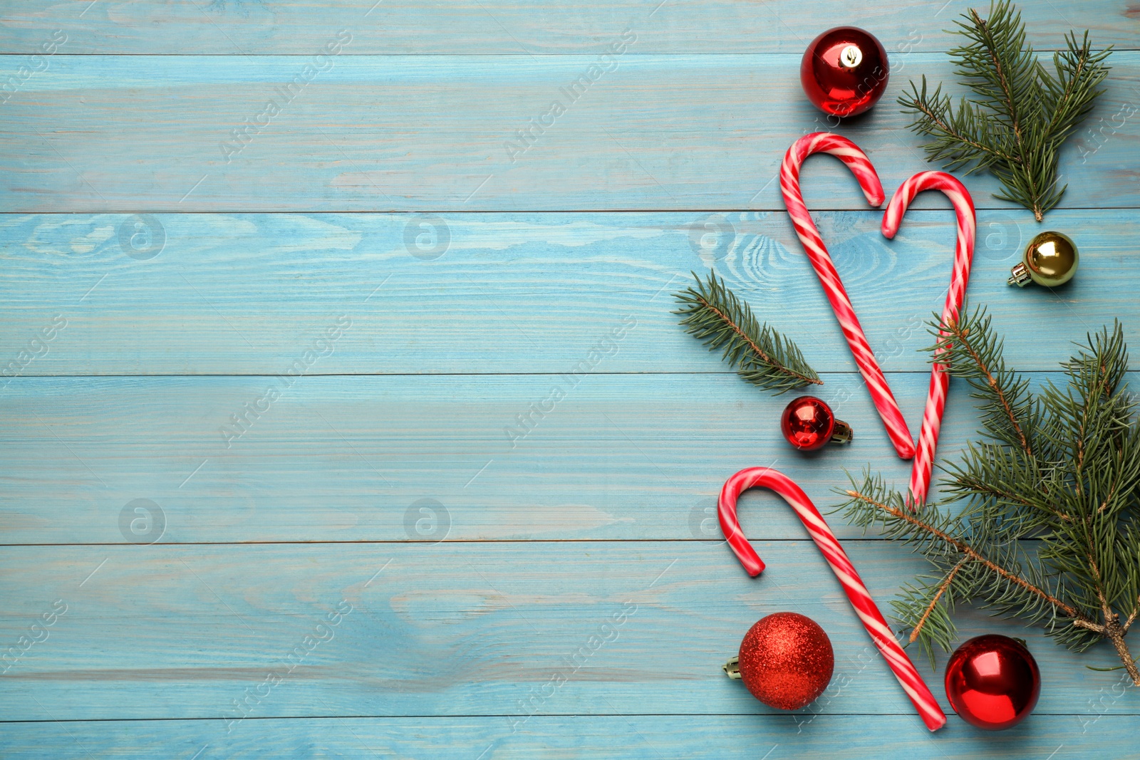 Photo of Tasty candy canes, fir branches and Christmas decor on light blue wooden table, flat lay. Space for text