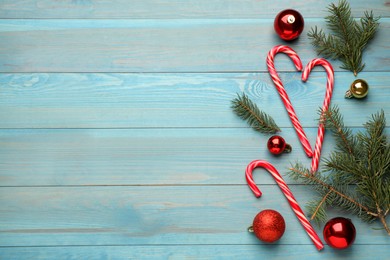 Tasty candy canes, fir branches and Christmas decor on light blue wooden table, flat lay. Space for text