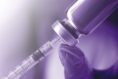 Doctor filling syringe with medication from vial, closeup. Color toned