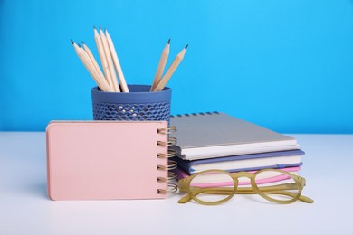 Photo of Different school stationery and glasses on white table against light blue background, space for text. Back to school