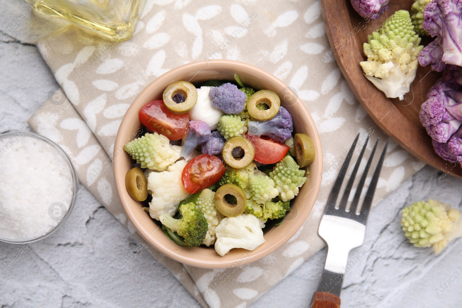 Photo of Delicious salad with cauliflower, tomato and olives served on white textured table, flat lay