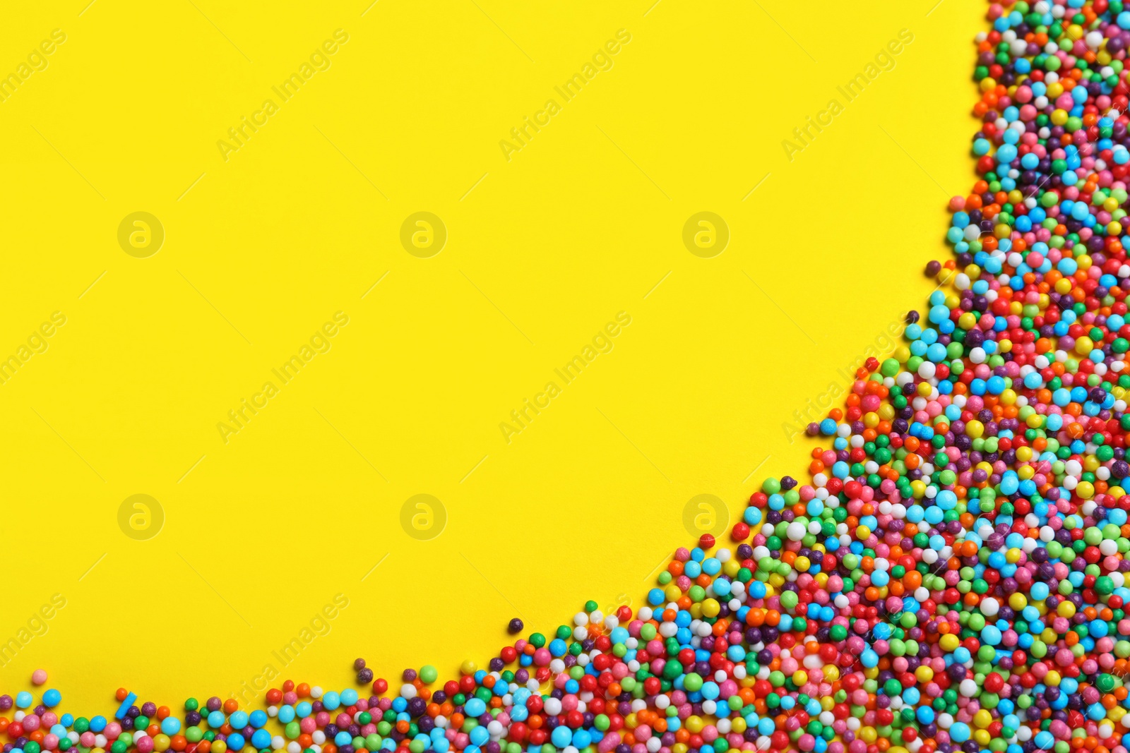 Photo of Bright colorful sprinkles on yellow background, flat lay with space for text. Confectionery decor