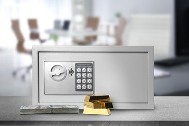 Closed steel safe with electronic lock, money and gold bars on grey table indoors