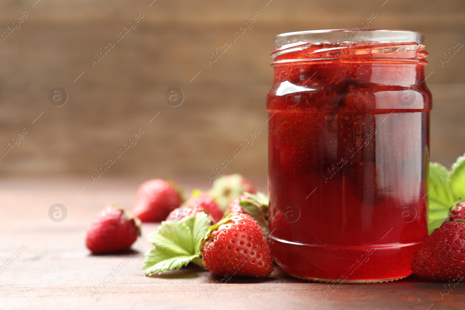 Photo of Delicious pickled strawberry jam and fresh berries on wooden table. Space for text