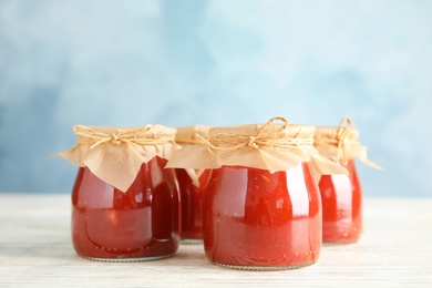 Photo of Jars of tomato sauce on wooden table against color background, space for text