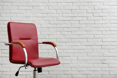 Photo of Comfortable office chair near white brick wall. Space for text