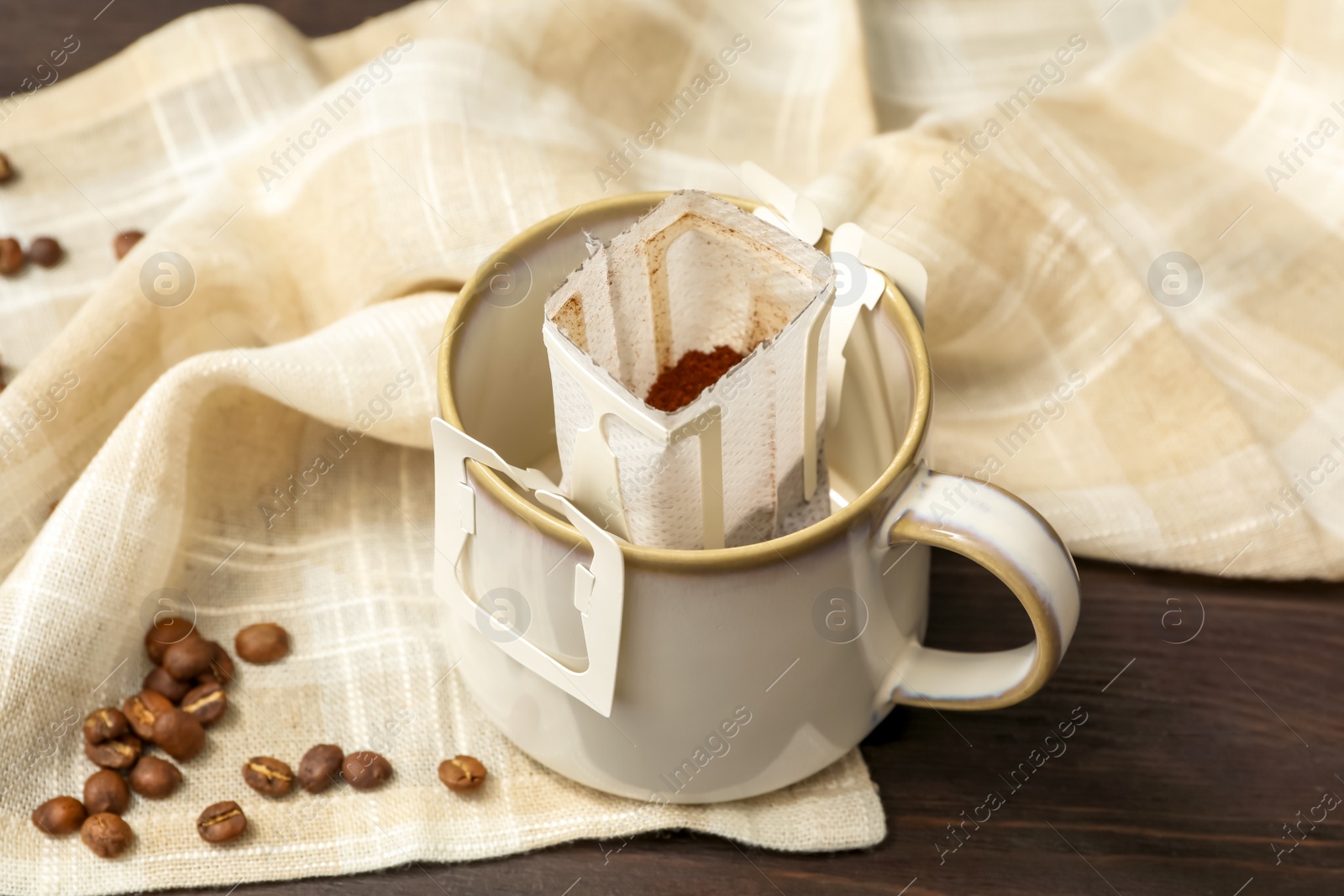 Photo of Drip coffee in cup and beans on brown wooden table, closeup