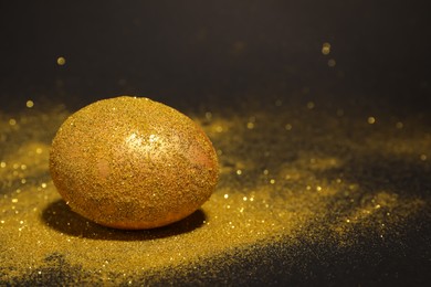 Shiny golden egg with glitter on dark table, space for text