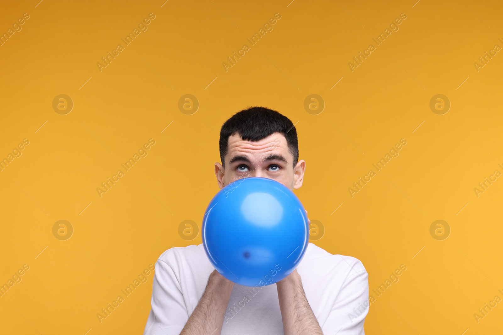 Photo of Young man inflating light blue balloon on yellow background