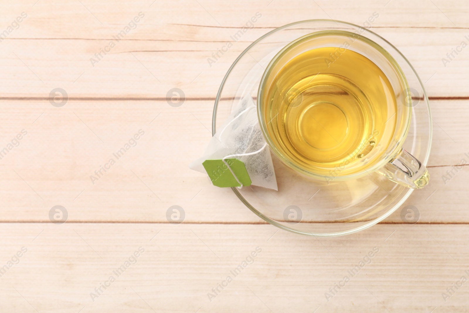 Photo of Tea bag and glass cup on light wooden table, top view. Space for text
