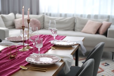 Beautiful table setting with burning candles and pink accent in dining room