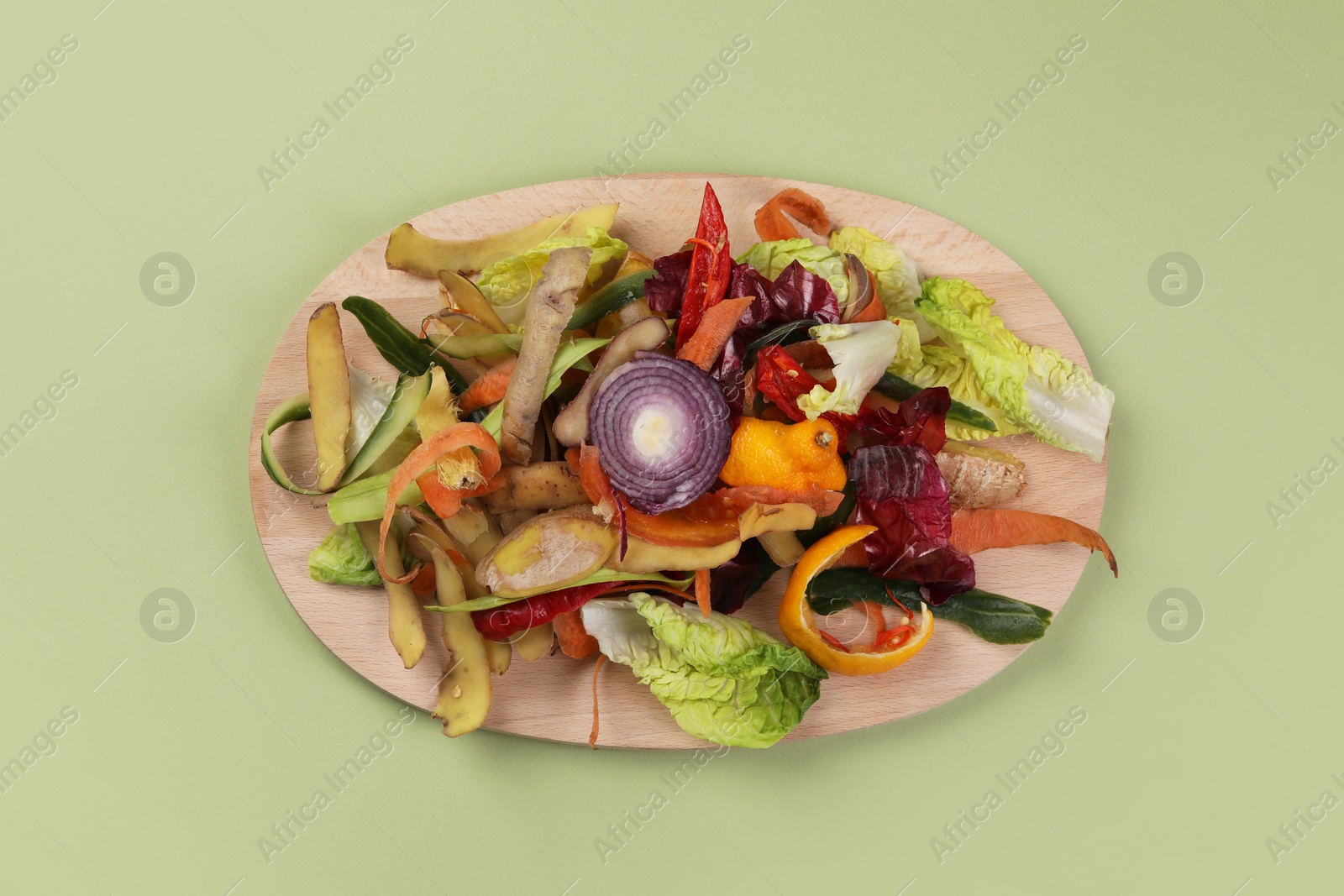 Photo of Peels of fresh vegetables with wooden board on light green background, top view